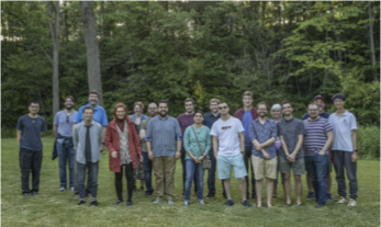 Members of the Vera Gorbunova laboratory gathered outdoors at the edge of a wooded area.